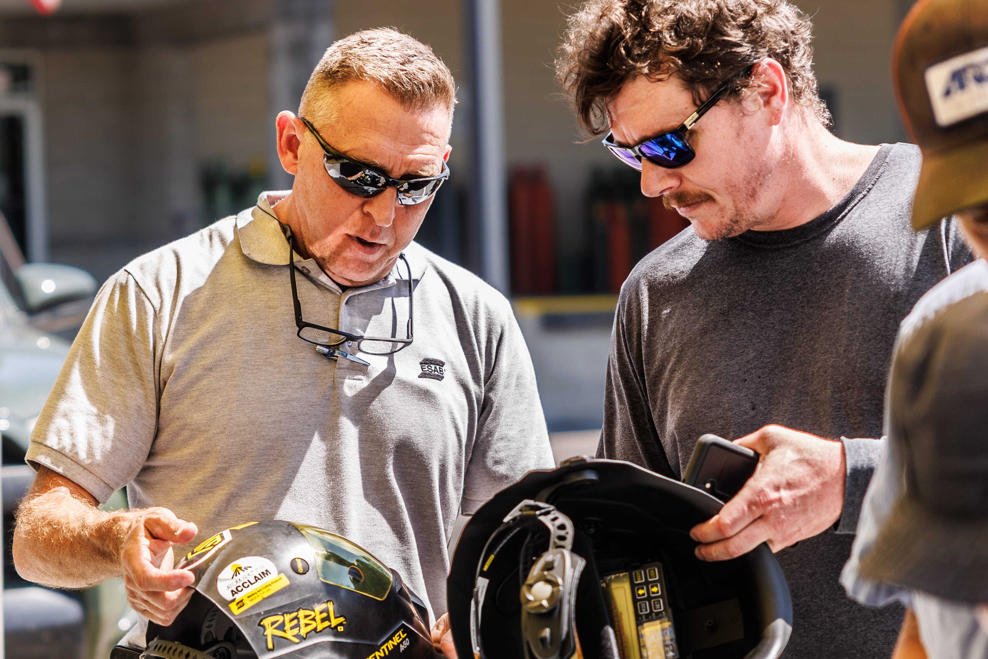 Welders discuss helmets at the ESAB Demo Tour, showcasing live welding demos and safety gear in a hands-on environment.