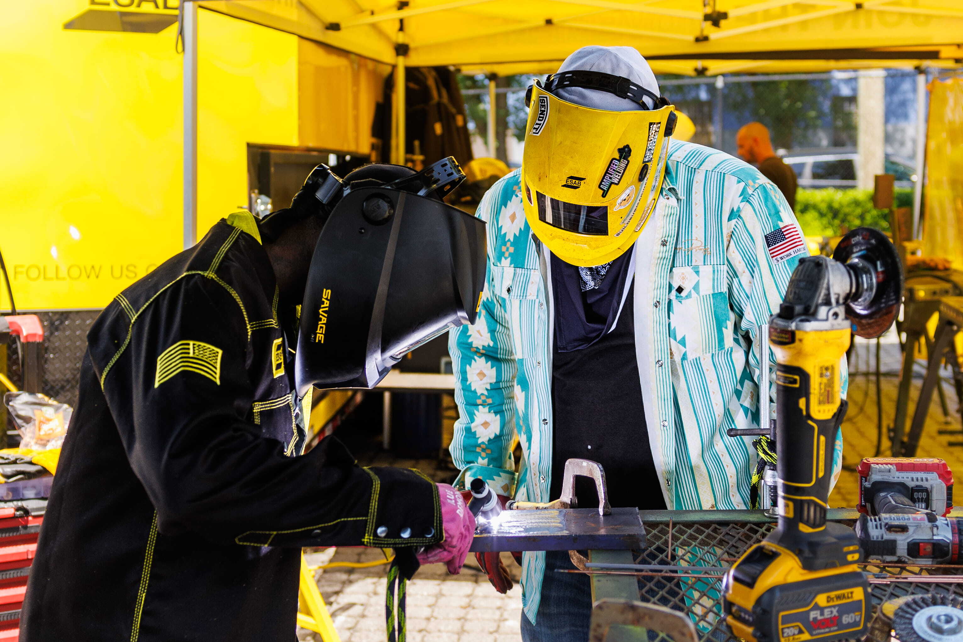 Welders in action at the ESAB Demo Tour, showcasing live welding demos under a bright yellow tent, focused on precision.